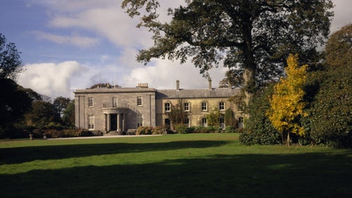 View of the east front of Arlington Court in Devon, showing the Greek revival house to the left and the servants' wing to the right surrounded by autumn colour.